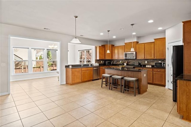 kitchen with a center island, brown cabinetry, a chandelier, backsplash, and appliances with stainless steel finishes