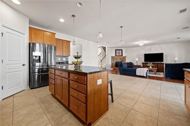 kitchen featuring a center island, brown cabinetry, light tile patterned floors, stainless steel fridge, and visible vents