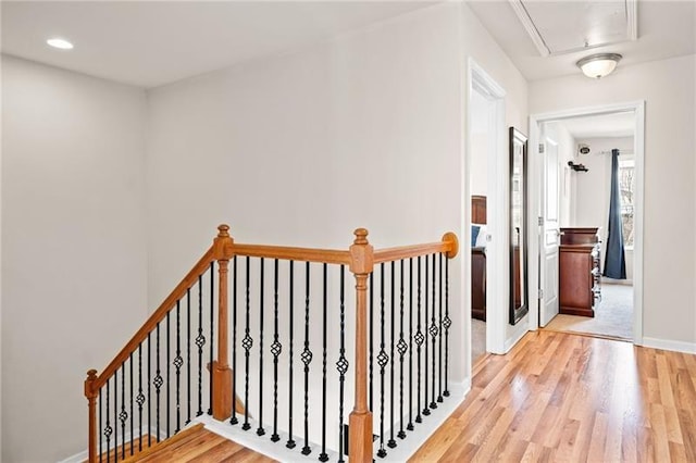 hall with attic access, wood finished floors, baseboards, and an upstairs landing
