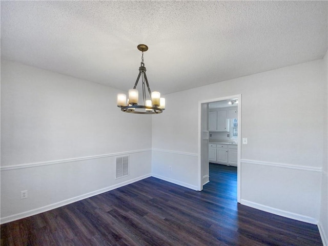 unfurnished dining area featuring a textured ceiling, dark hardwood / wood-style flooring, and a notable chandelier