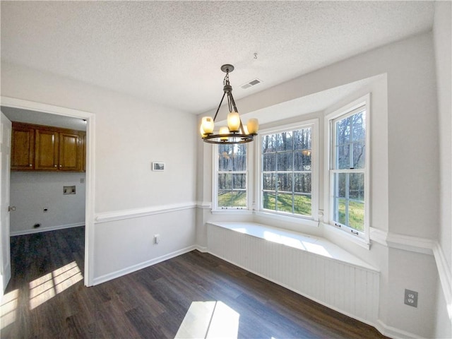 unfurnished dining area with a textured ceiling, dark wood-type flooring, and a notable chandelier