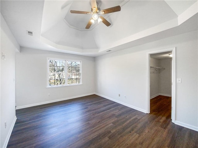 unfurnished bedroom with a walk in closet, a raised ceiling, ceiling fan, and dark wood-type flooring