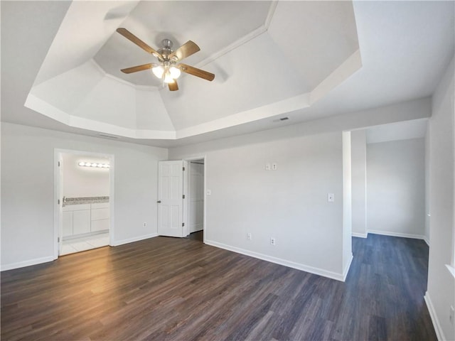 empty room with dark hardwood / wood-style flooring, a tray ceiling, vaulted ceiling, and ceiling fan