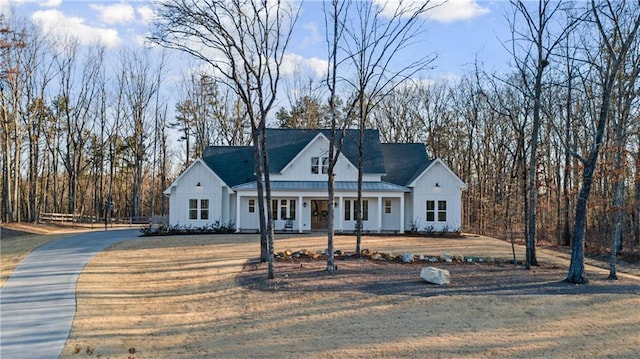 modern farmhouse with a standing seam roof, covered porch, a front lawn, board and batten siding, and metal roof