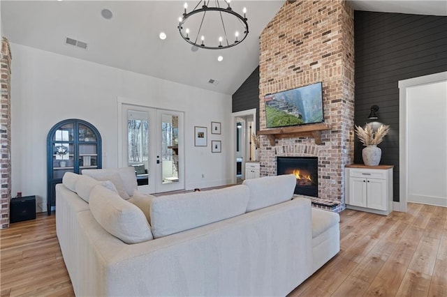 living room with high vaulted ceiling, a fireplace, visible vents, and light wood-type flooring