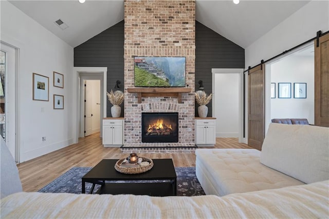 living room with visible vents, high vaulted ceiling, a barn door, light wood-style floors, and a fireplace