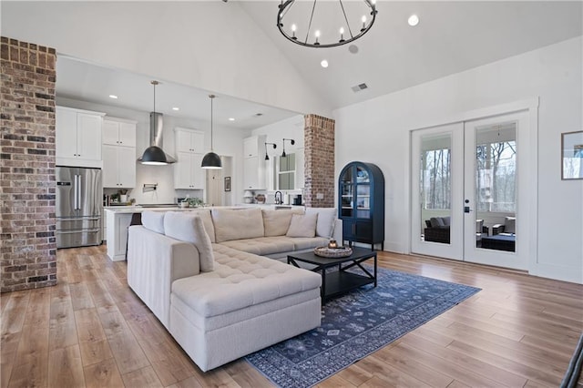 living area featuring visible vents, high vaulted ceiling, light wood-style flooring, french doors, and a notable chandelier