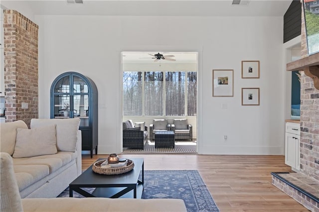 living room featuring visible vents, baseboards, ceiling fan, and light wood finished floors