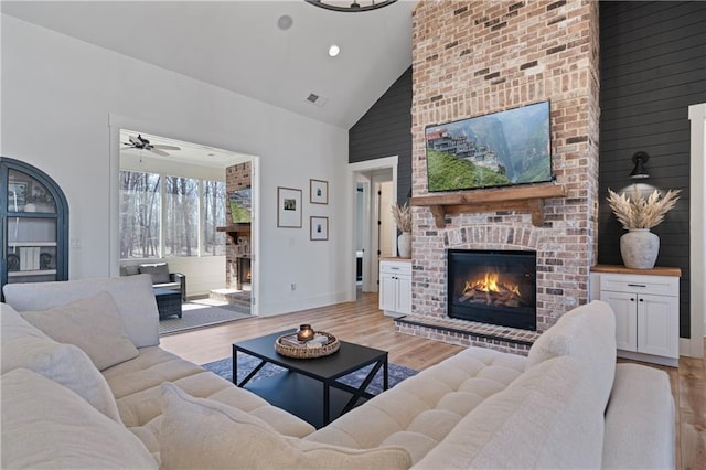 living area featuring light wood finished floors, a fireplace, high vaulted ceiling, and baseboards