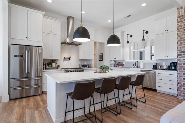 kitchen featuring light wood-style flooring, stainless steel appliances, wall chimney exhaust hood, and white cabinetry