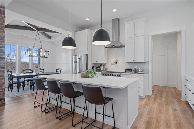 kitchen with light countertops, wall chimney range hood, light wood-style floors, and stainless steel appliances