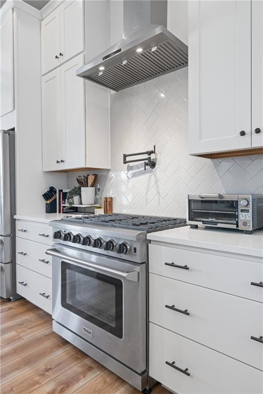 kitchen with light wood-style flooring, wall chimney range hood, white cabinetry, appliances with stainless steel finishes, and light countertops