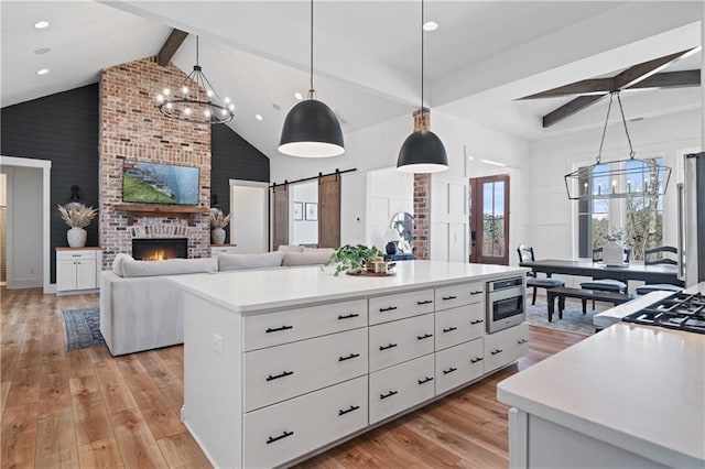 kitchen with light countertops, white cabinets, light wood-style floors, a barn door, and beamed ceiling