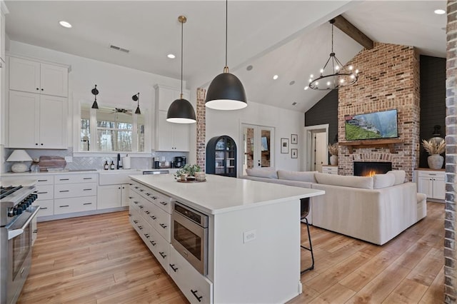 kitchen featuring beam ceiling, light wood-style flooring, a center island, and stainless steel appliances