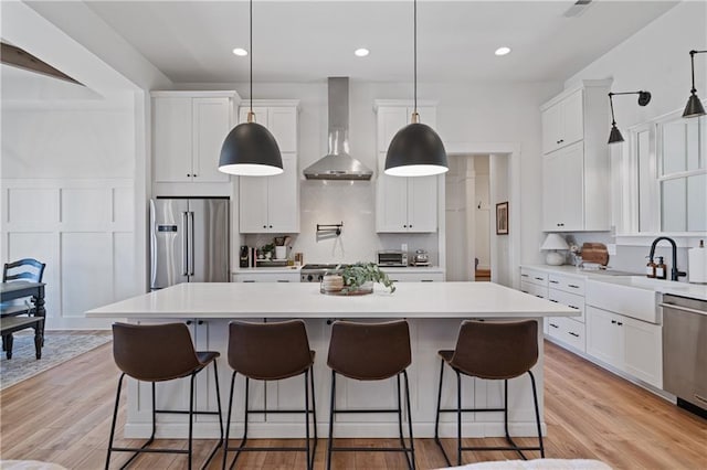 kitchen with stainless steel appliances, wall chimney exhaust hood, white cabinets, and light wood-style flooring