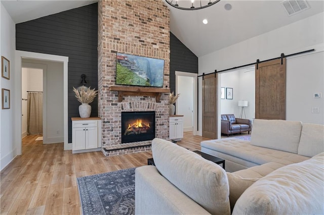 living room featuring a barn door, light wood-style flooring, visible vents, and high vaulted ceiling