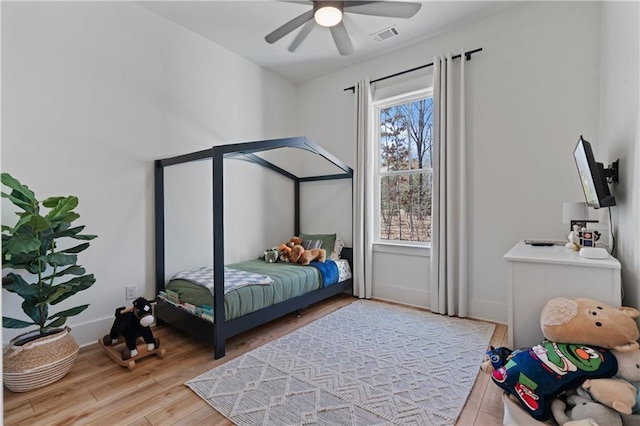 bedroom featuring a ceiling fan, light wood-style floors, visible vents, and baseboards