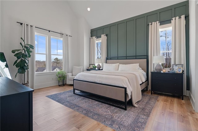 bedroom featuring light wood-type flooring, baseboards, and high vaulted ceiling