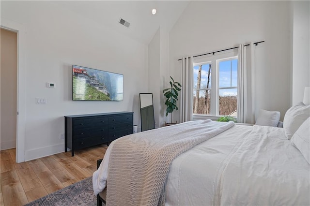 bedroom featuring baseboards, wood finished floors, visible vents, and high vaulted ceiling