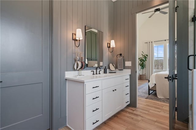 full bath featuring wooden walls, ceiling fan, vanity, wood finished floors, and ensuite bath