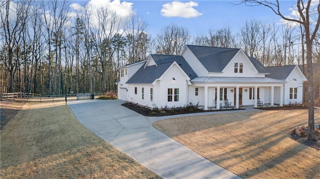 modern farmhouse featuring fence, a porch, concrete driveway, a front yard, and metal roof