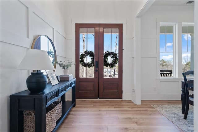 entrance foyer with a decorative wall, french doors, light wood finished floors, and a healthy amount of sunlight