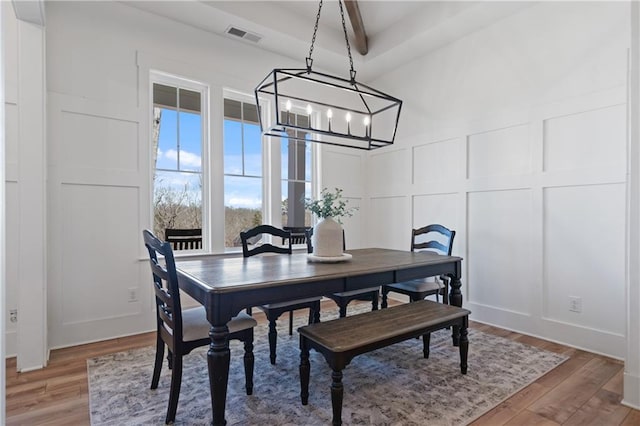 dining space with a decorative wall, a notable chandelier, light wood-style floors, and visible vents