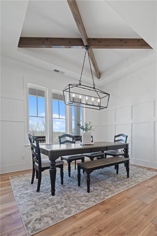 dining space featuring light wood-type flooring, visible vents, beamed ceiling, and a decorative wall