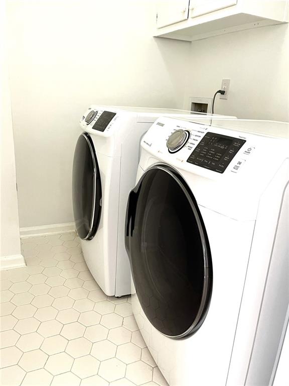 laundry area featuring light tile patterned flooring, washing machine and dryer, and cabinets