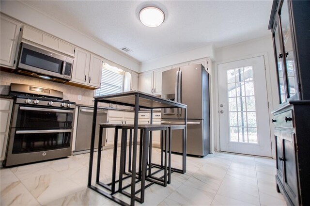 kitchen with backsplash, a wealth of natural light, white cabinetry, and stainless steel appliances