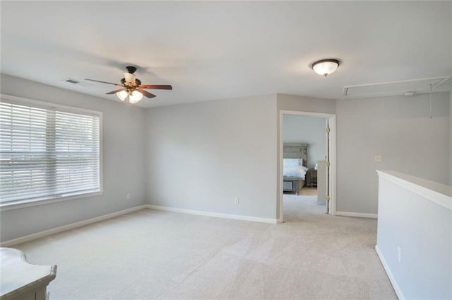 spare room with light colored carpet, attic access, visible vents, ceiling fan, and baseboards