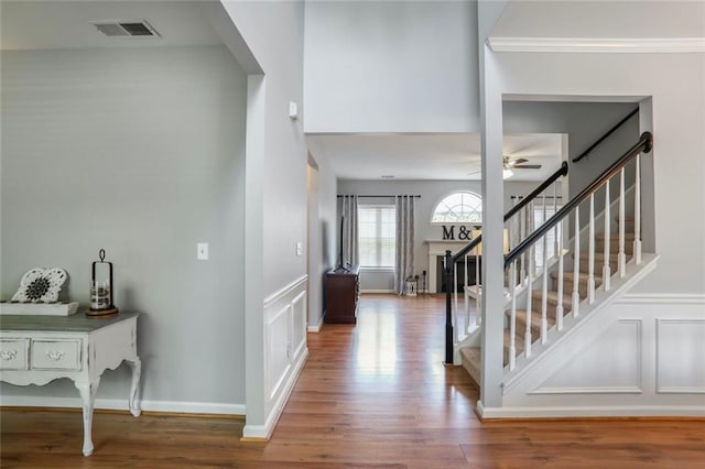 foyer entrance featuring a decorative wall, a ceiling fan, visible vents, and wood finished floors