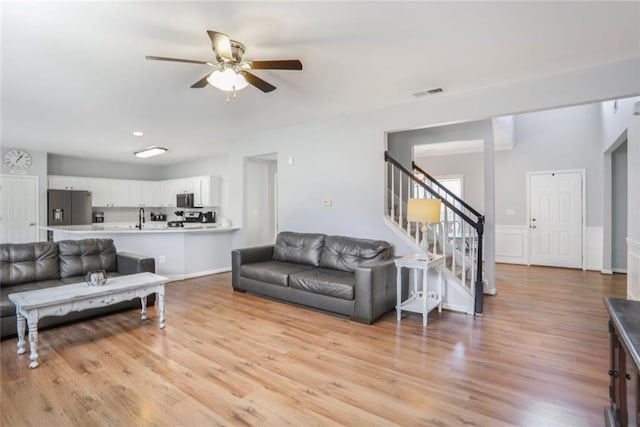 living room featuring ceiling fan, stairway, light wood finished floors, and visible vents