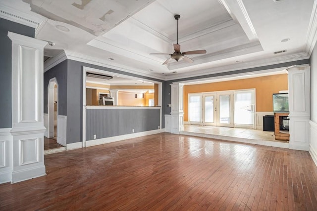 unfurnished living room featuring a tray ceiling, wood-type flooring, ceiling fan, and ornate columns