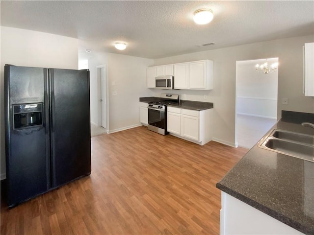 kitchen with white cabinets, light wood finished floors, appliances with stainless steel finishes, a sink, and an inviting chandelier