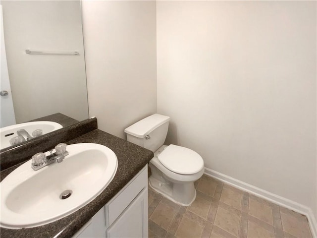 half bath featuring toilet, vanity, stone finish flooring, and baseboards