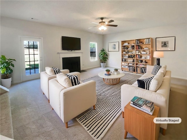 carpeted living room with plenty of natural light, baseboards, a fireplace with flush hearth, and a ceiling fan