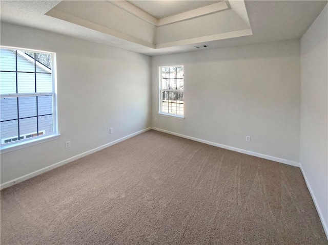 empty room with a tray ceiling, baseboards, and carpet