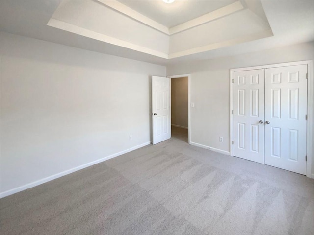 unfurnished bedroom with a tray ceiling, baseboards, a closet, and carpet floors