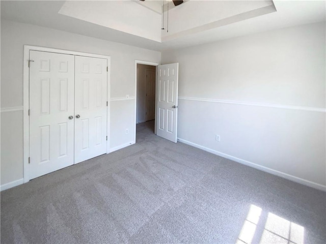 unfurnished bedroom featuring a tray ceiling, a closet, carpet floors, a ceiling fan, and baseboards