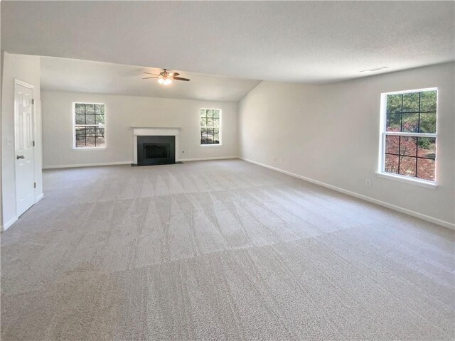 unfurnished living room with a fireplace with flush hearth, a textured ceiling, carpet, baseboards, and ceiling fan
