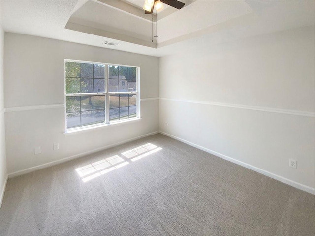 carpeted spare room with a tray ceiling, baseboards, and a ceiling fan