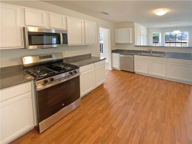 kitchen with a sink, dark countertops, light wood finished floors, white cabinets, and appliances with stainless steel finishes