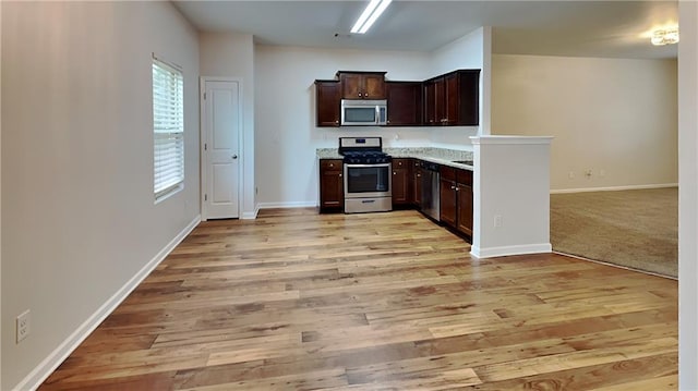 kitchen featuring dark brown cabinets, appliances with stainless steel finishes, light hardwood / wood-style floors, and light stone countertops