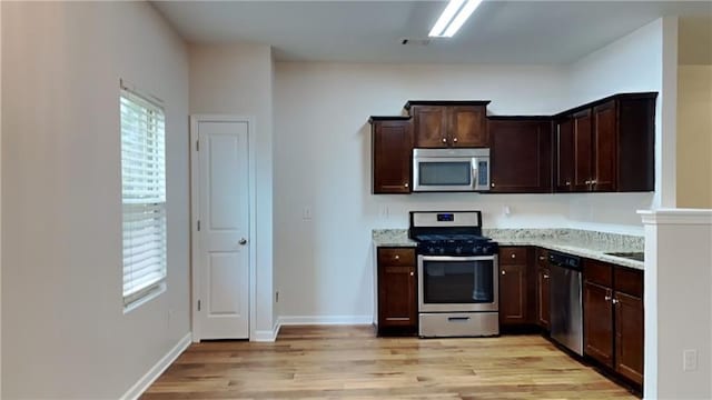 kitchen featuring light wood-type flooring, appliances with stainless steel finishes, dark brown cabinets, and light stone countertops