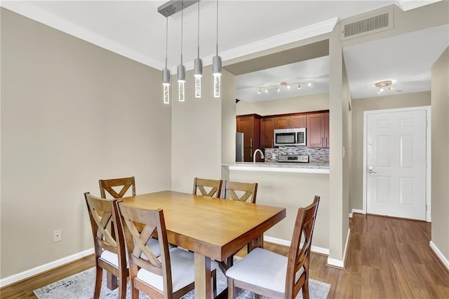 dining room with ornamental molding, wood finished floors, visible vents, and baseboards