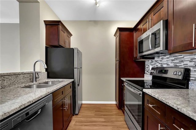 kitchen featuring baseboards, a sink, stainless steel appliances, tasteful backsplash, and light wood-type flooring