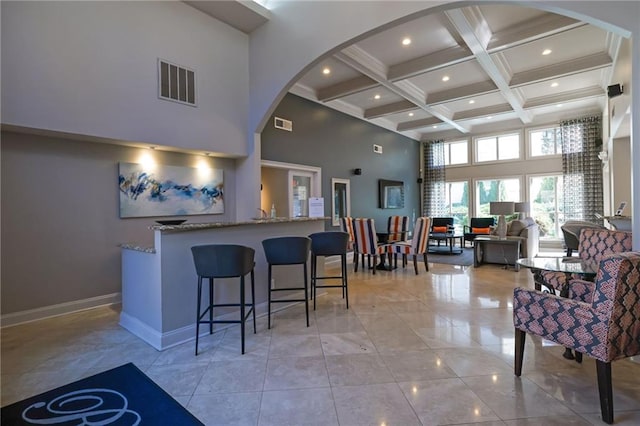 kitchen with visible vents, beam ceiling, coffered ceiling, a high ceiling, and stone counters