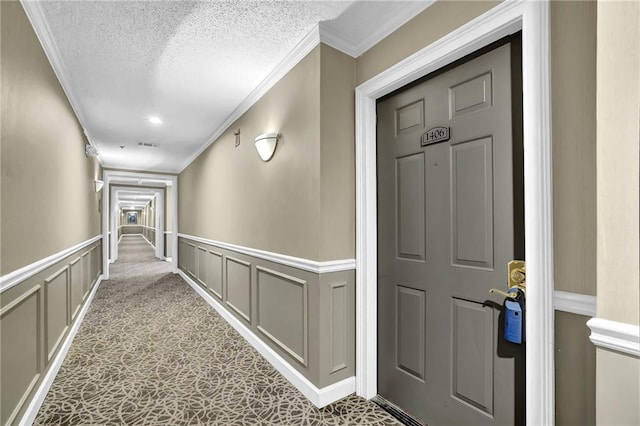 corridor featuring a wainscoted wall, visible vents, a textured ceiling, crown molding, and a decorative wall