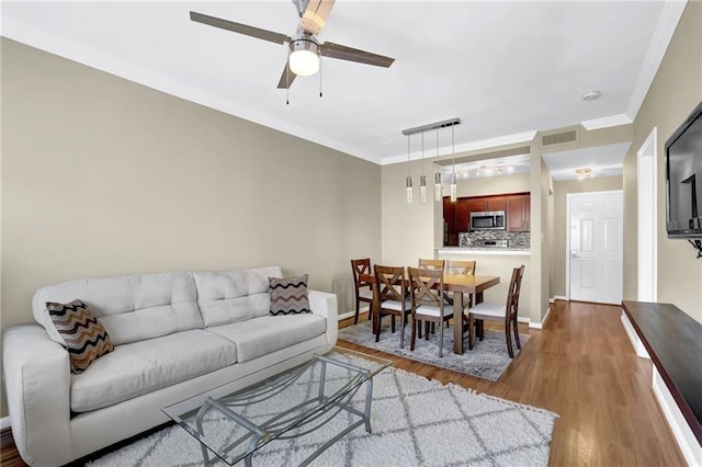 living room with wood finished floors, baseboards, visible vents, ceiling fan, and crown molding